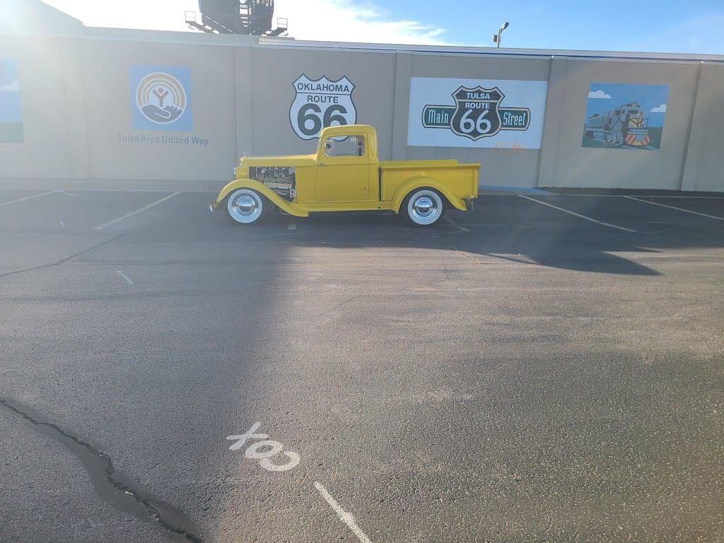 Yellow vintage truck parked in front of Route 66 mural, sunny day.