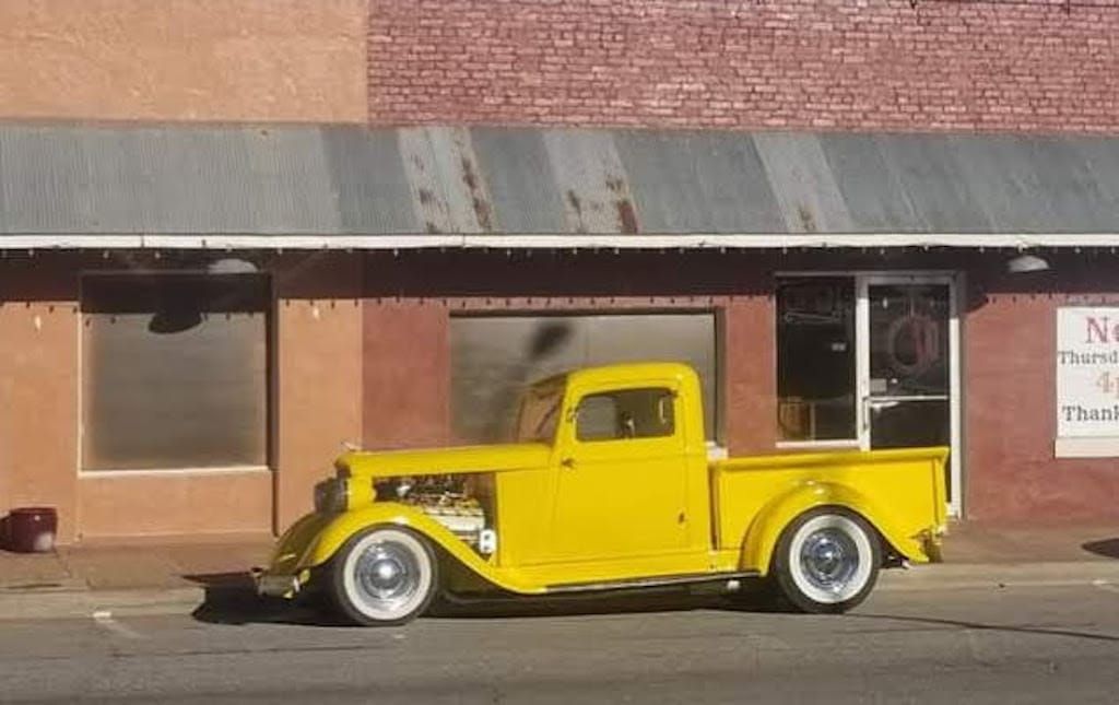 Yellow vintage pickup truck parked in front of a brick building.