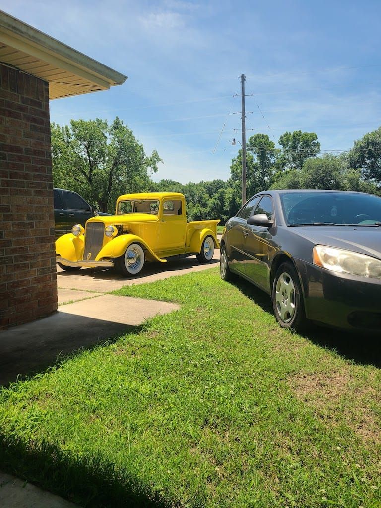 Yellow vintage truck parked next to a gray car on a sunny day.