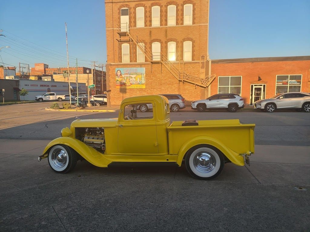 Yellow vintage pickup truck parked on street in front of brick buildings.