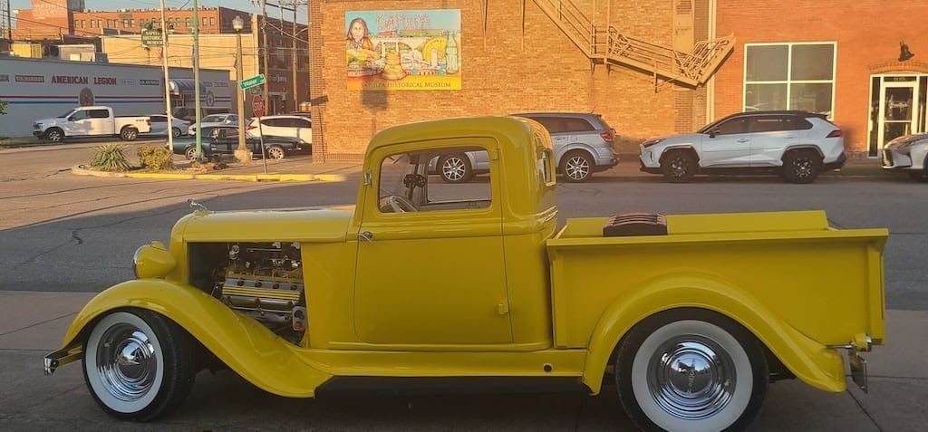 Yellow vintage pickup truck parked on the street. Brown brick building in the background.