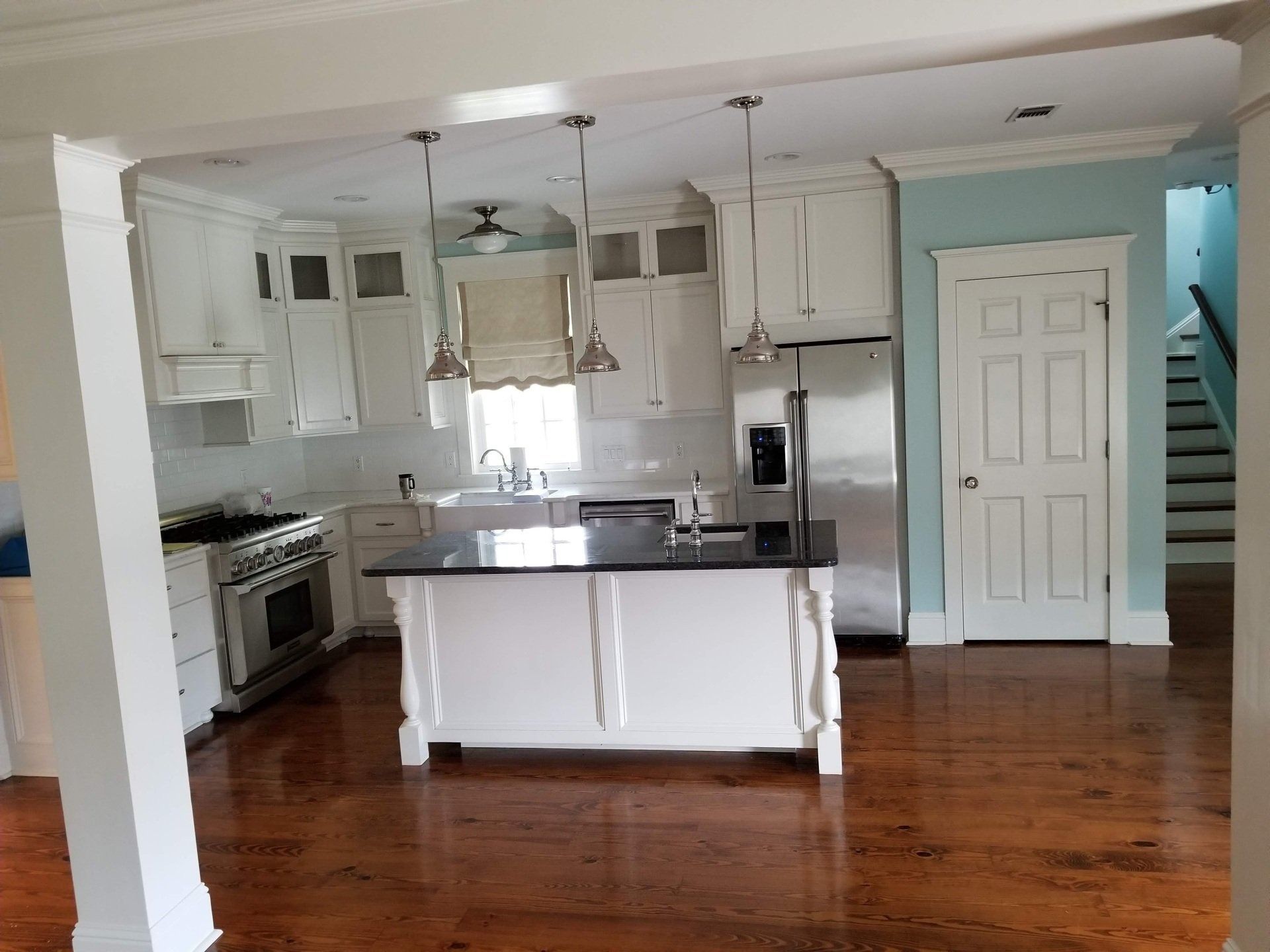 Kitchen with white cabinets, stainless steel appliances, dark countertop island, and wood floors.