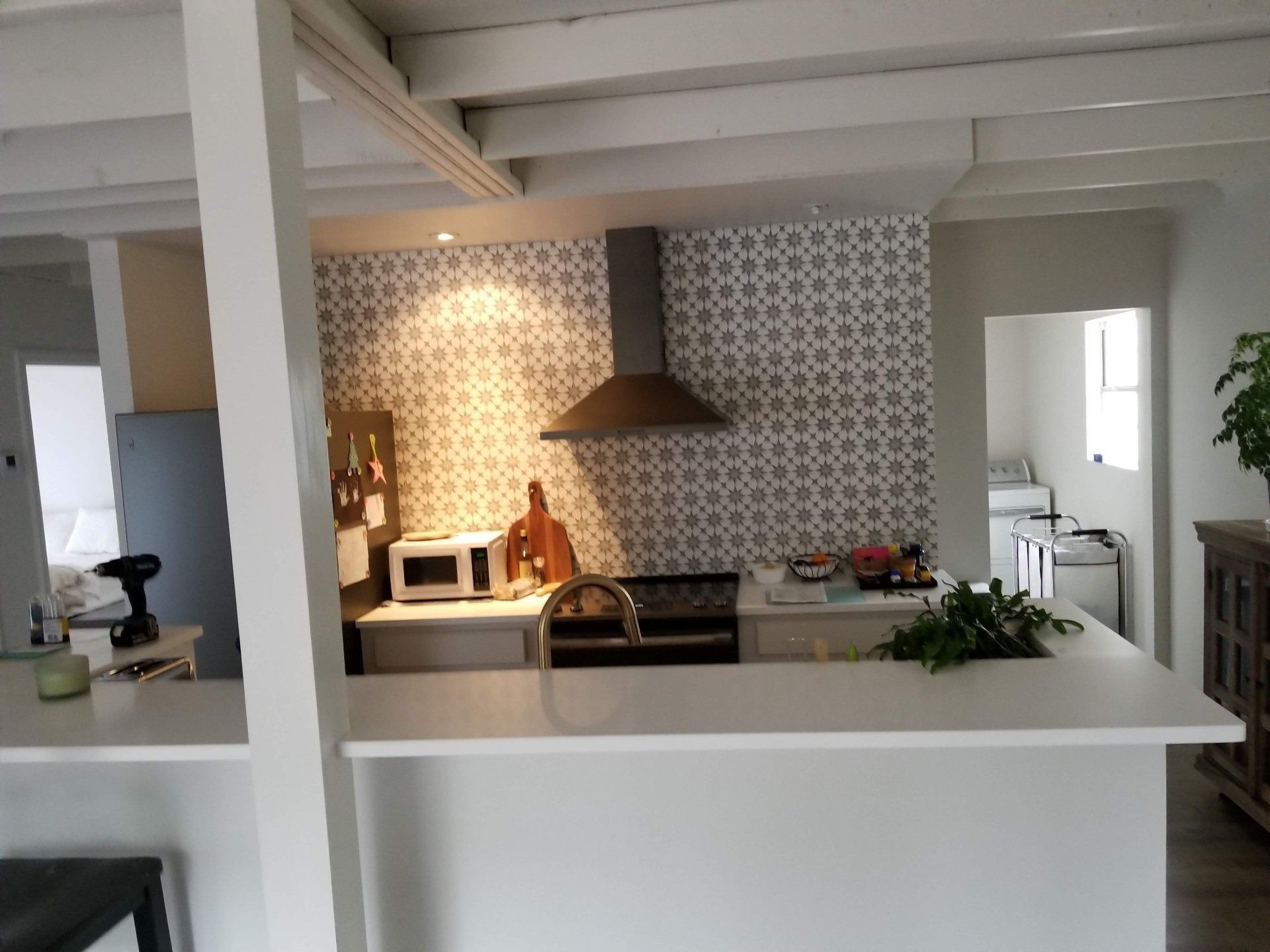 Kitchen with white countertops, patterned backsplash, range hood, and overhead beams.