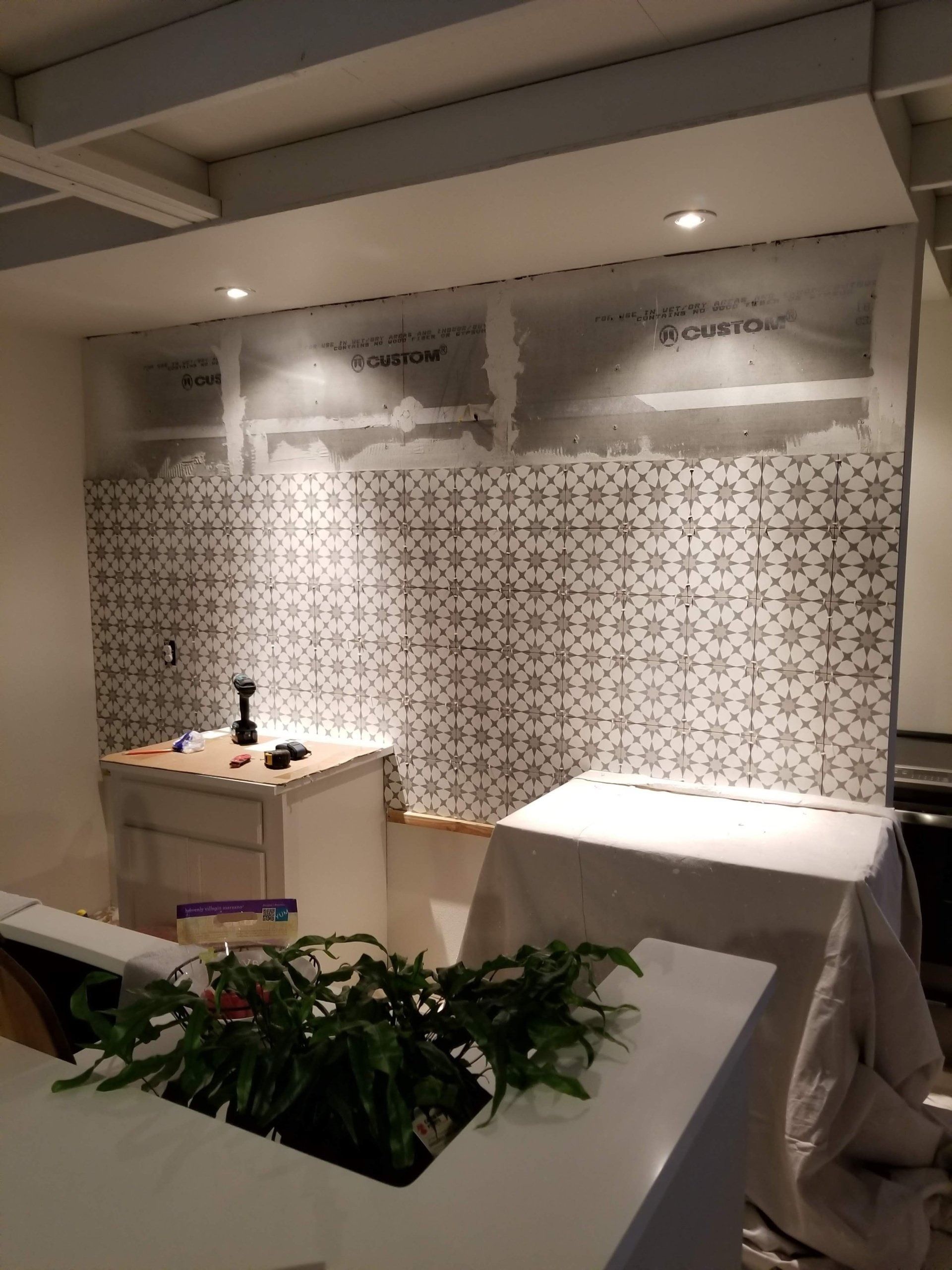 Bathroom under renovation; tiled wall, cabinets, white coverings, overhead lighting.