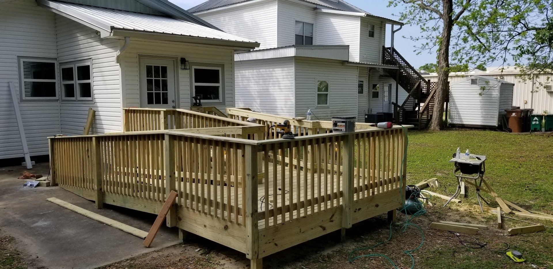 A wooden ramp with railings leading to a white building with windows. Trees and grass in the background.
