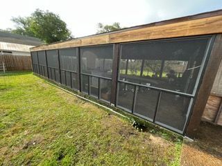 Long, screened-in structure with wooden trim, set in a grassy yard.