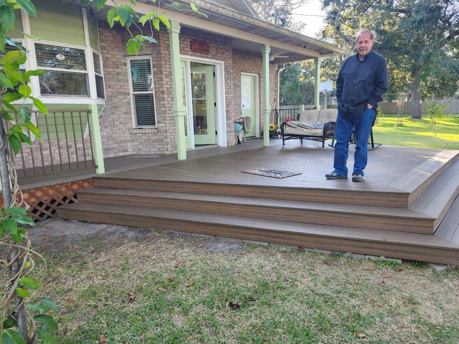 Man stands on a new wood deck in front of a house. The deck has three steps, and the house has a porch.