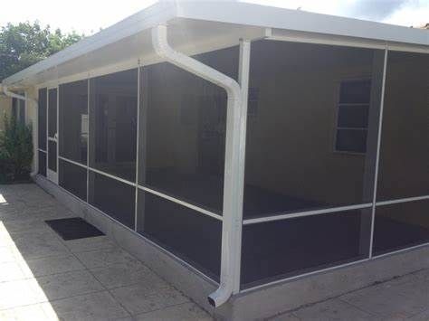Screened porch with white frame, white roof, and tan wall, on a paved patio.