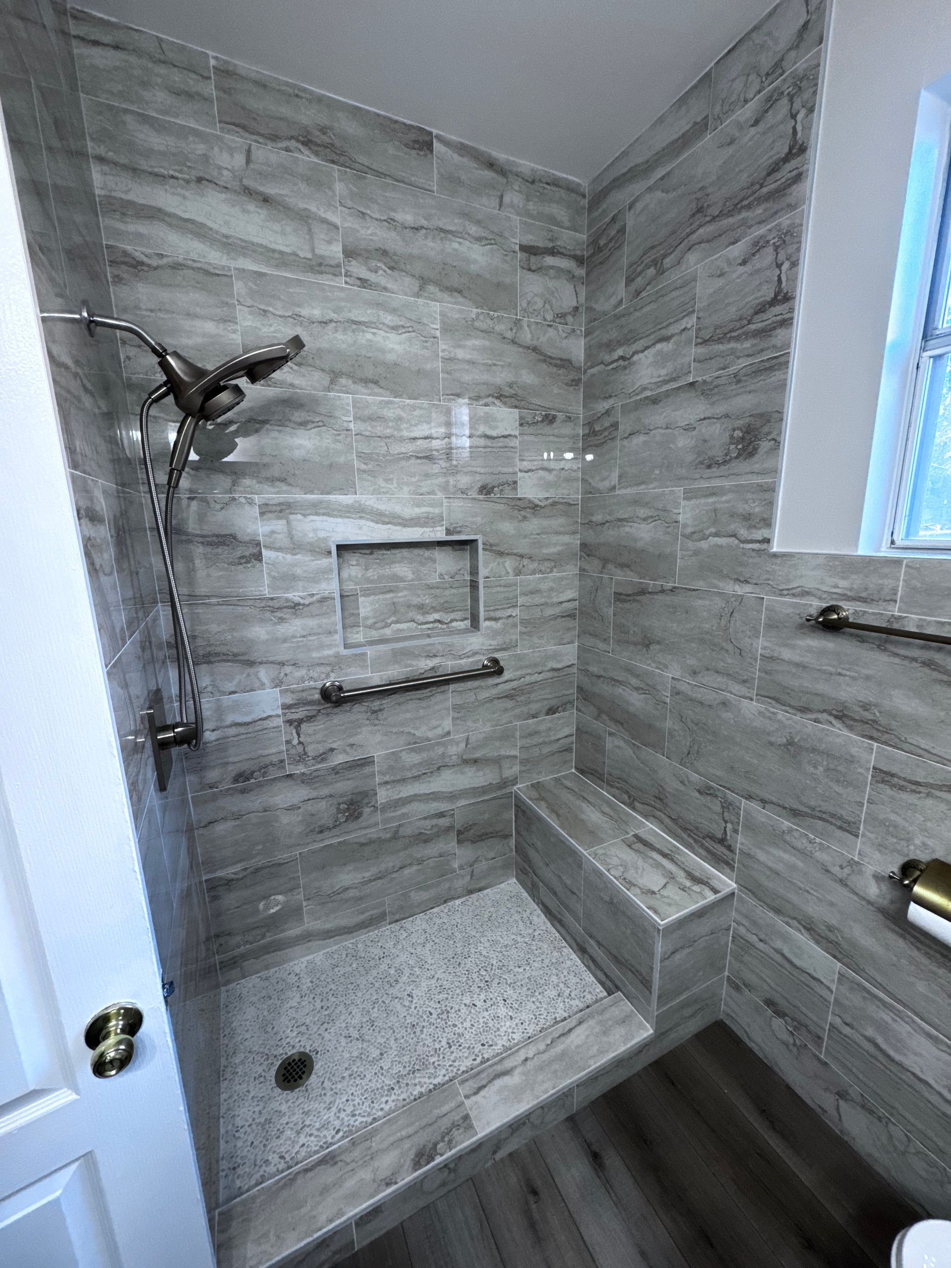 Modern gray-tiled shower with built-in bench, niche, and rainfall showerhead.