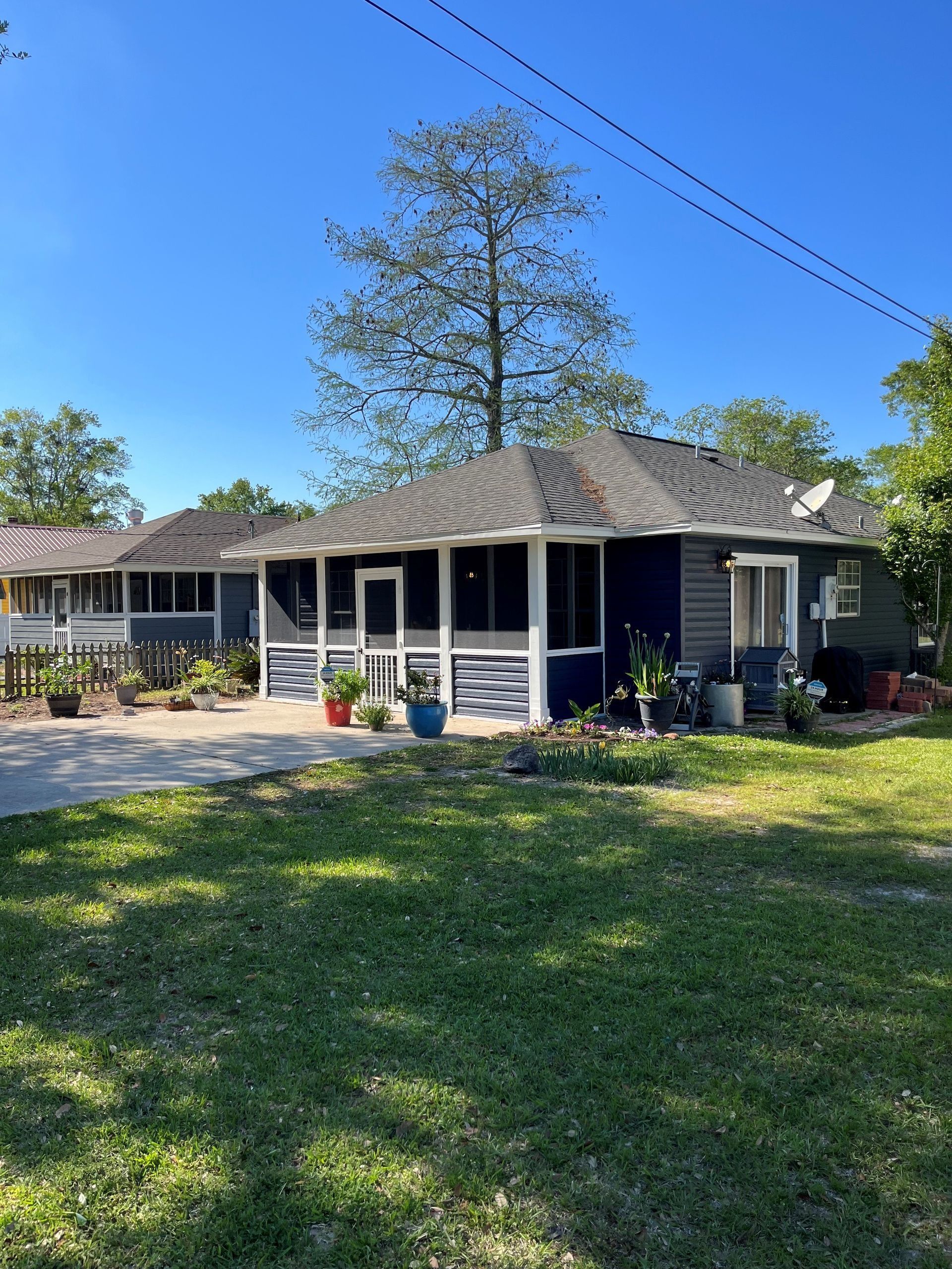 Blue house with screened-in porch, potted plants, and driveway, under a clear blue sky.
