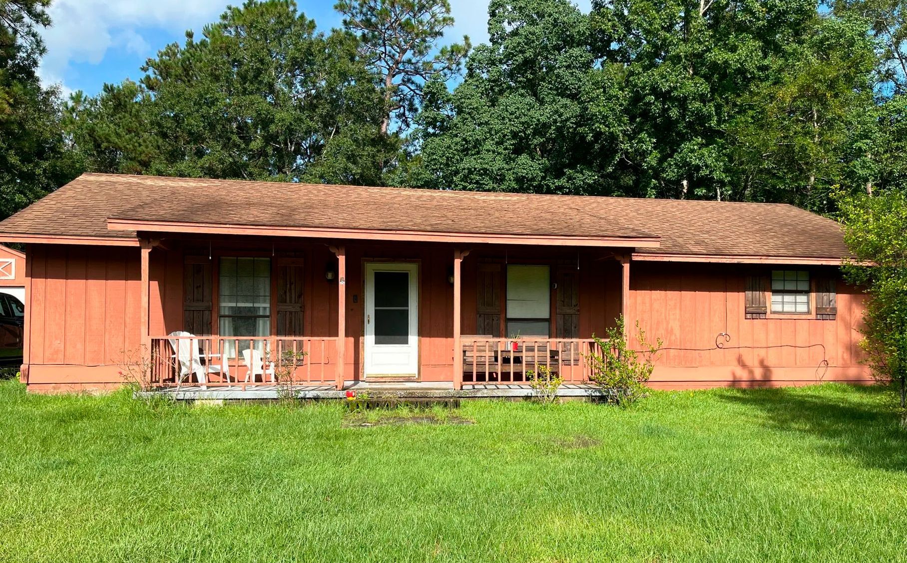 A single-story, orange house with a porch and overgrown yard; trees in the background.