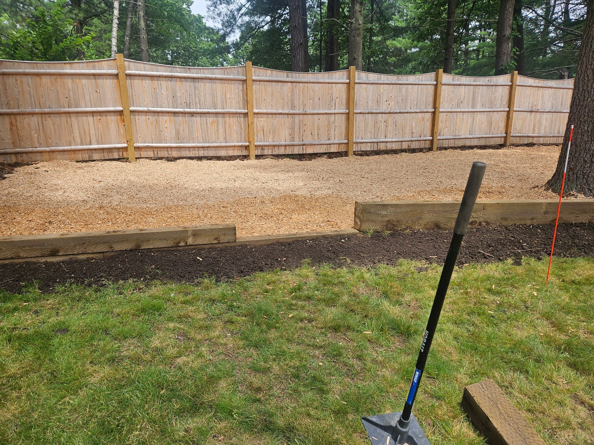 a shovel is sitting in the grass in front of a wooden fence