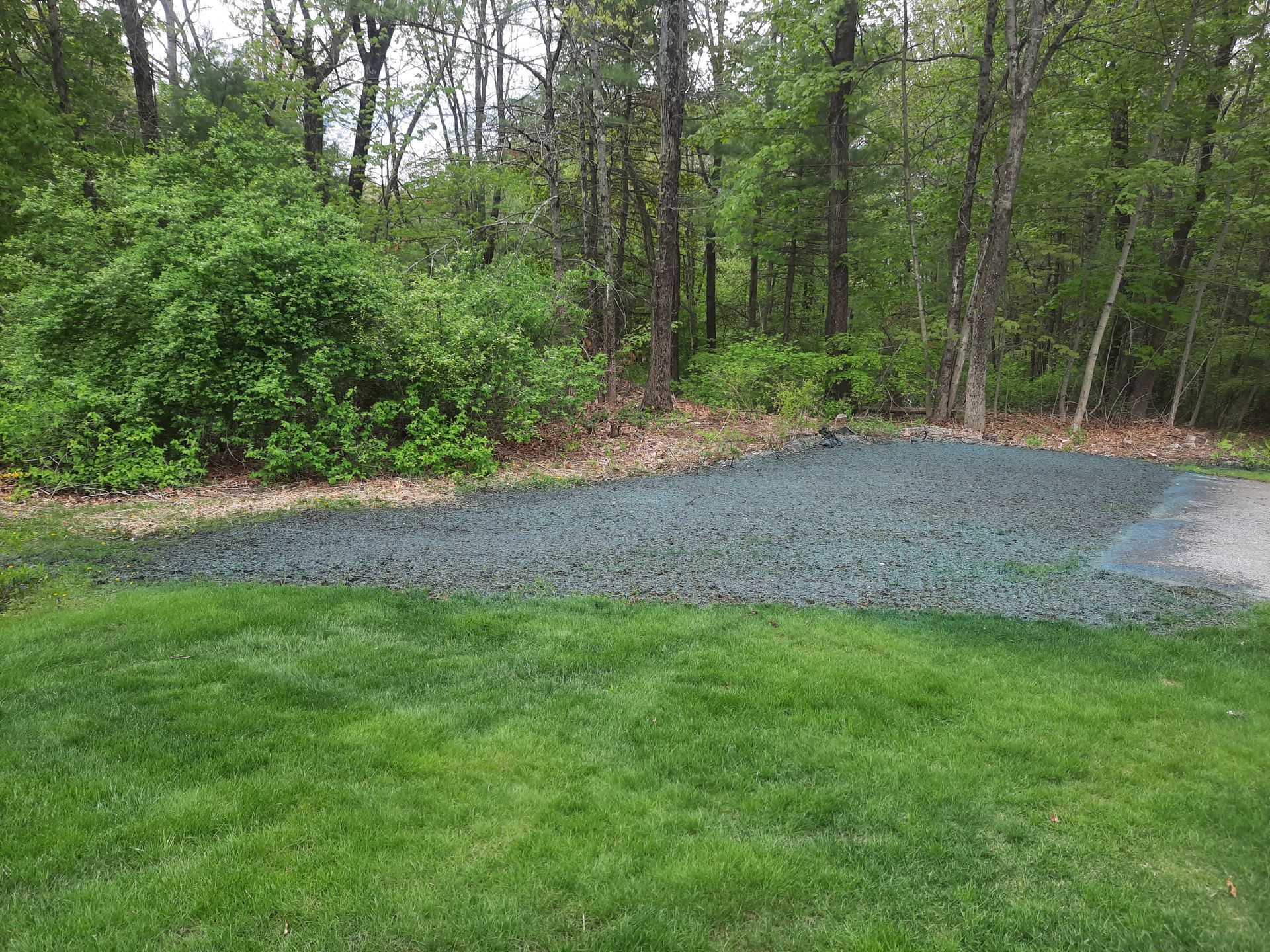 a lush green lawn with trees in the background and gravel in the foreground .