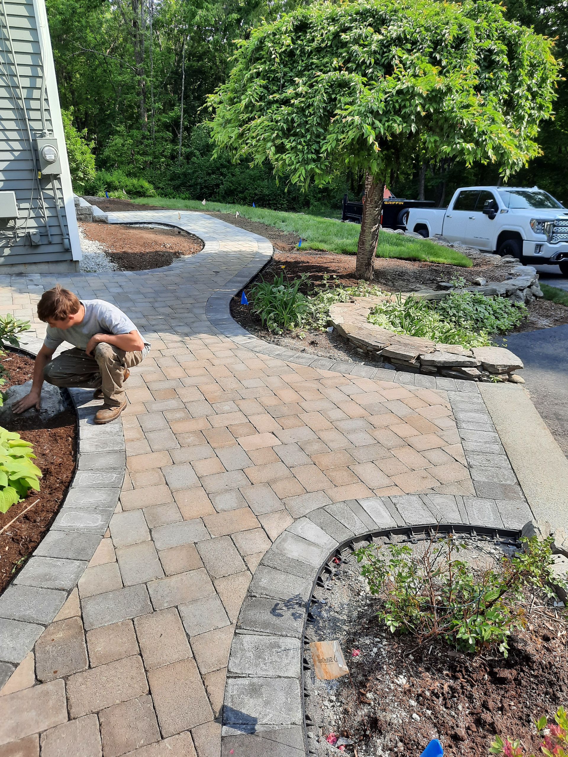 a man is working on a brick walkway in a garden