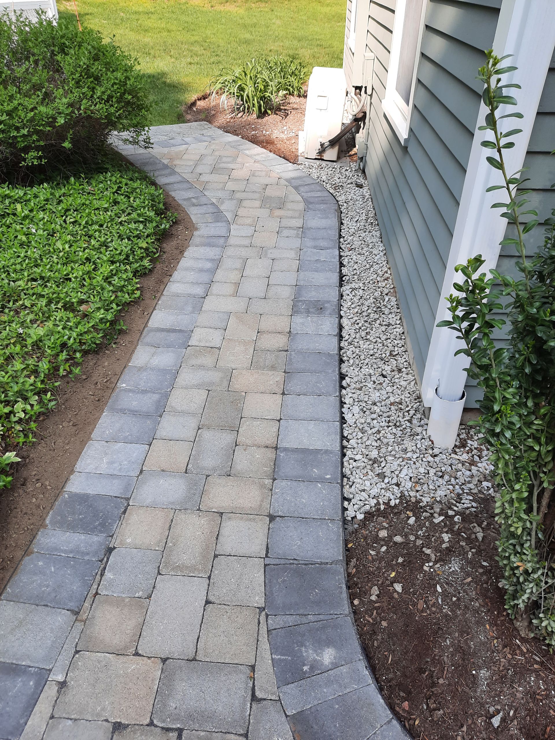 a brick walkway leading to a house with gravel on the side