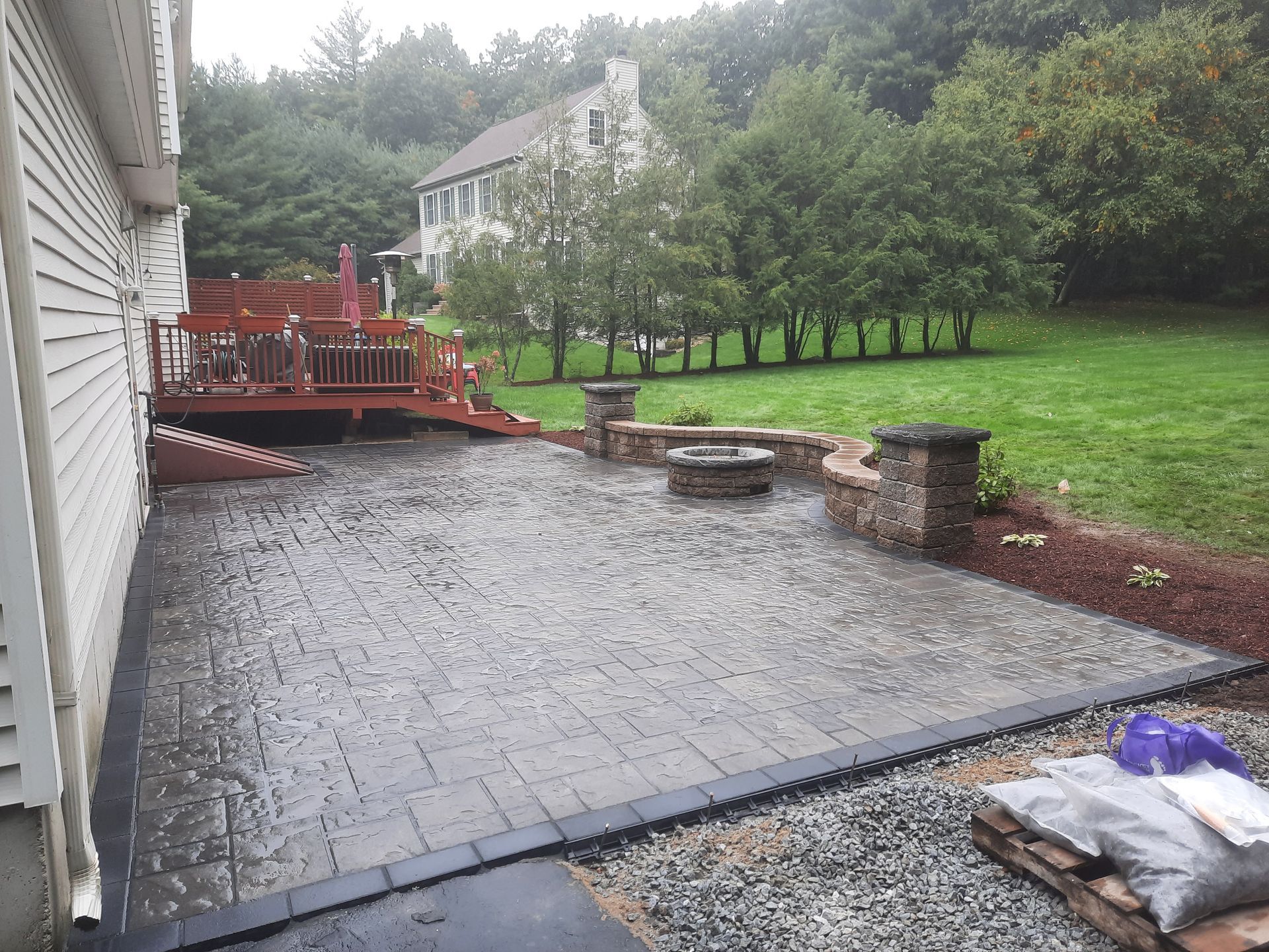 a patio with a fire pit and a deck in the background