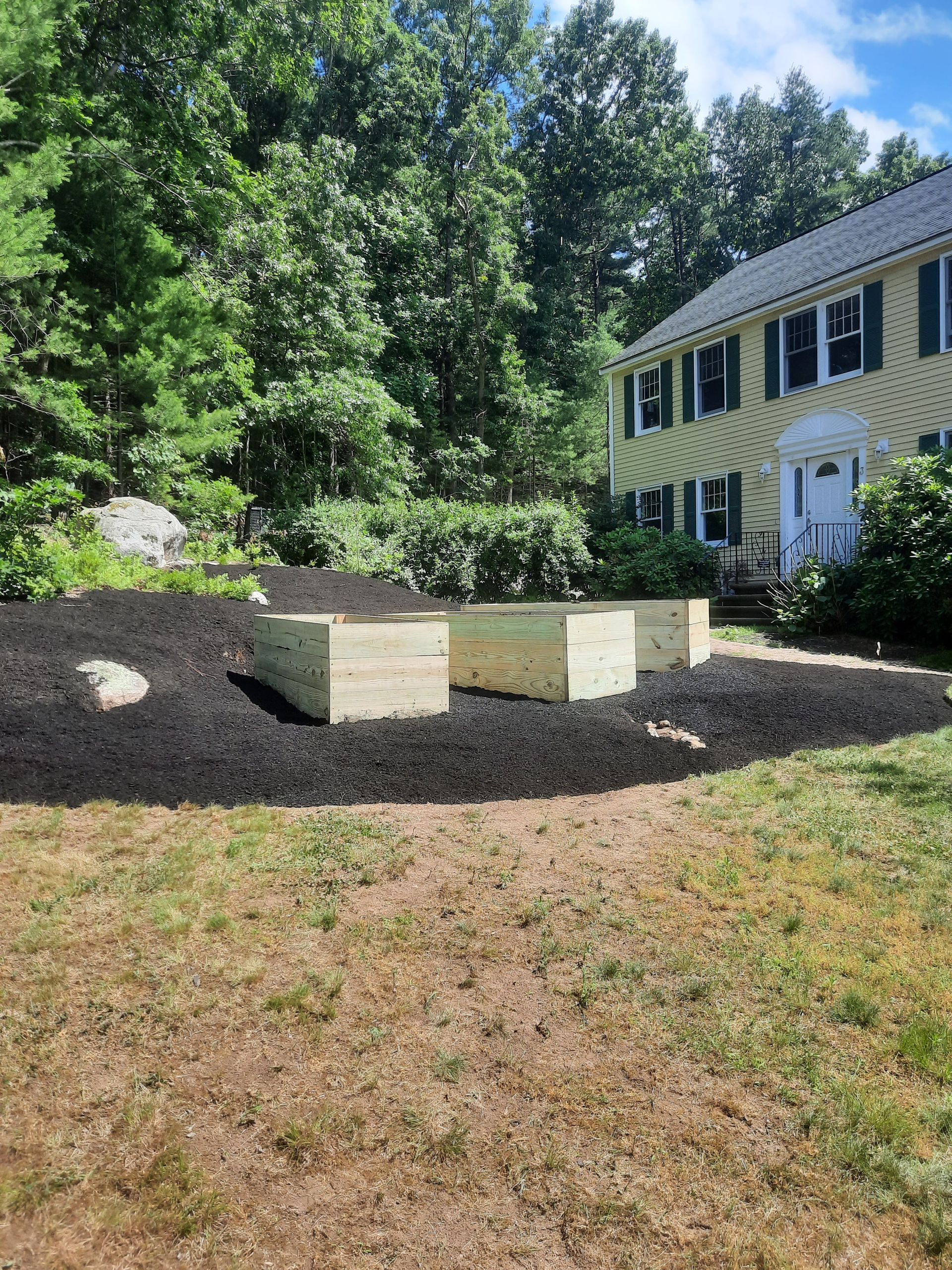 a house with a lot of trees in the background and a wooden planter in front of it .