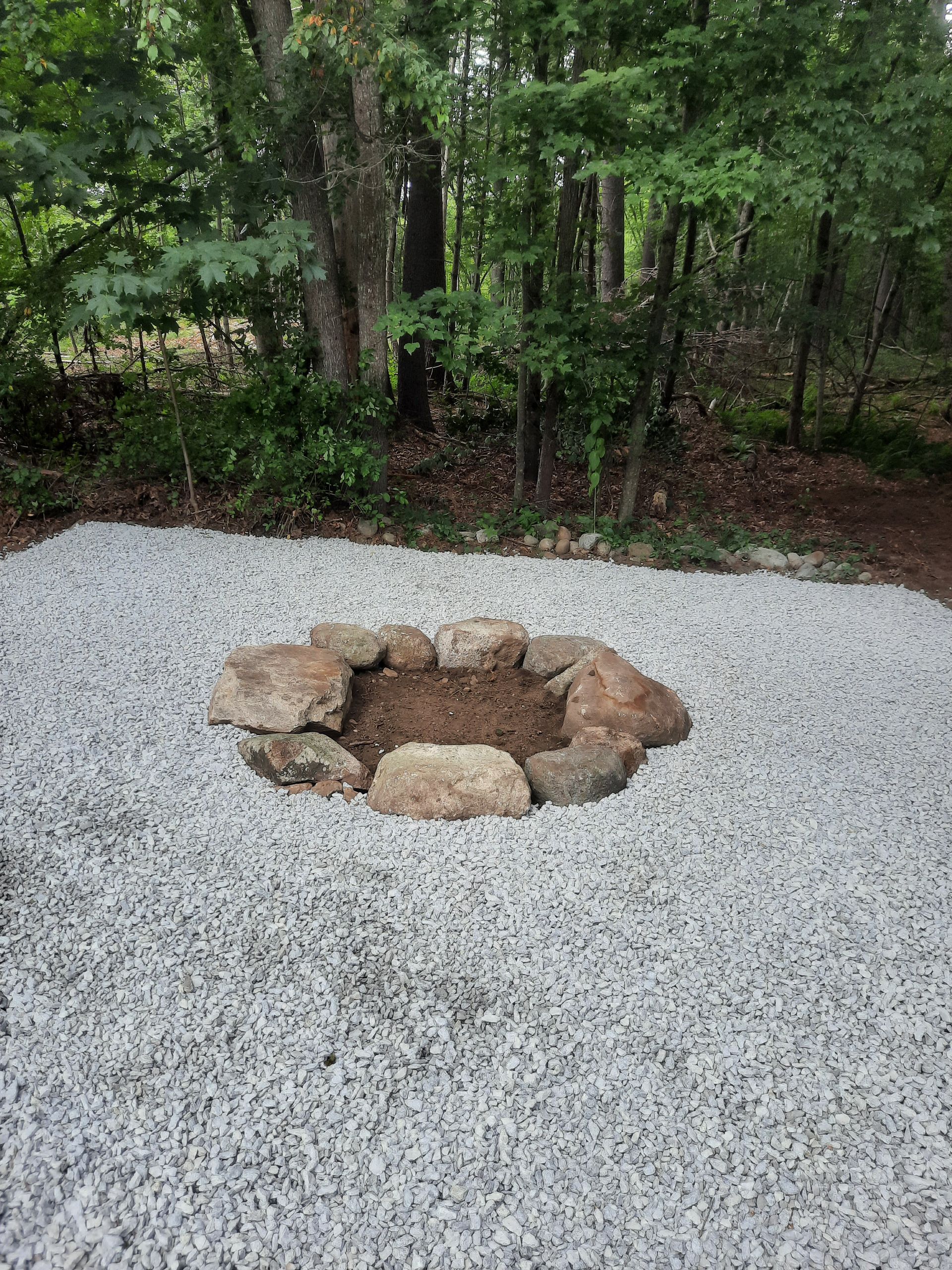 a fire pit is surrounded by gravel in the middle of a forest