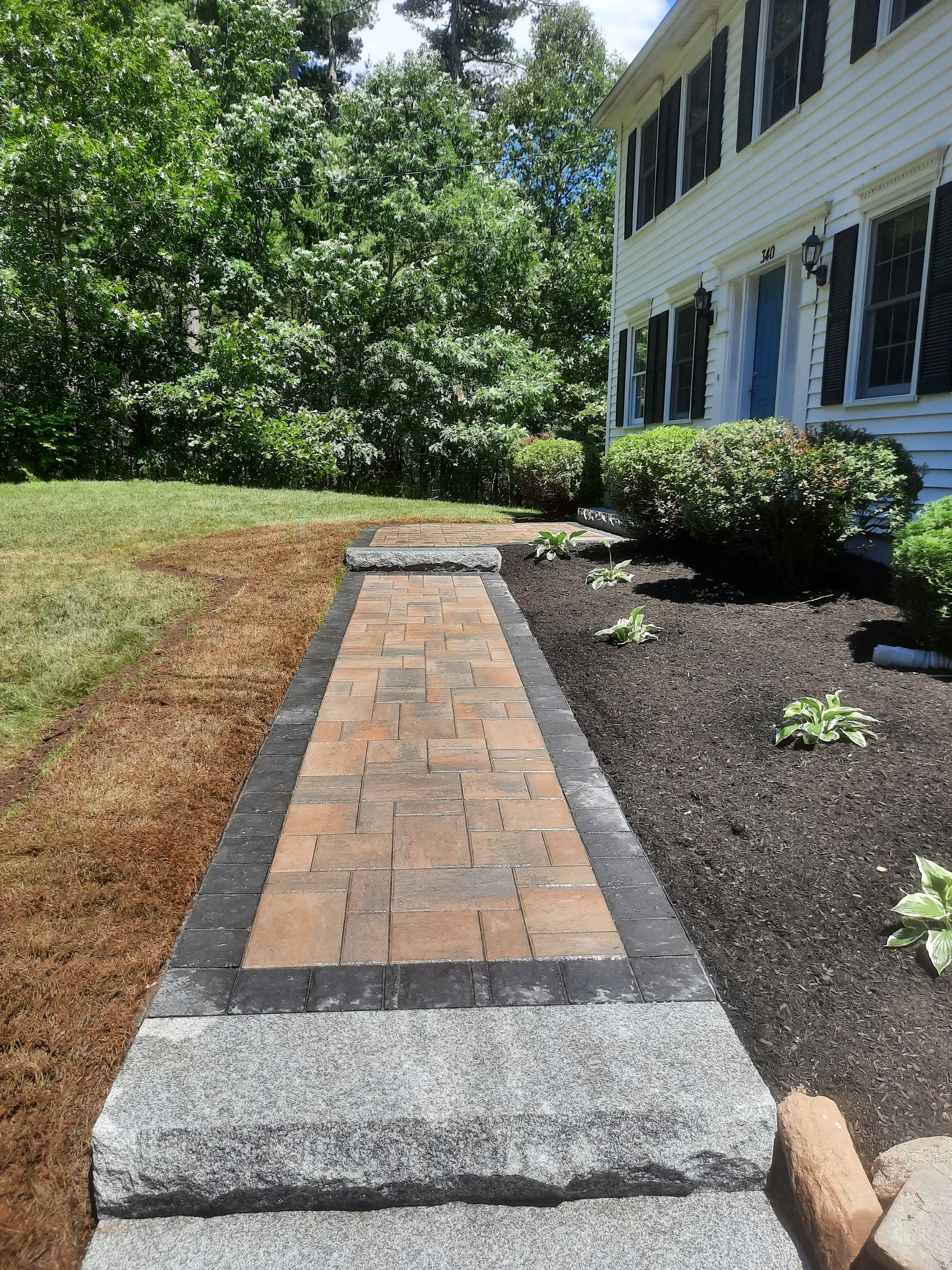 a brick walkway leading to a house with trees in the background
