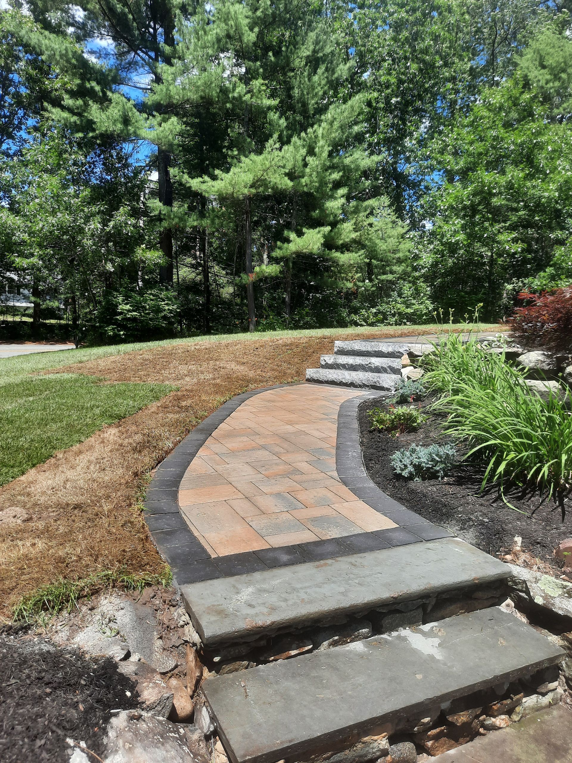 a brick walkway with steps leading up to a lush green field surrounded by trees .