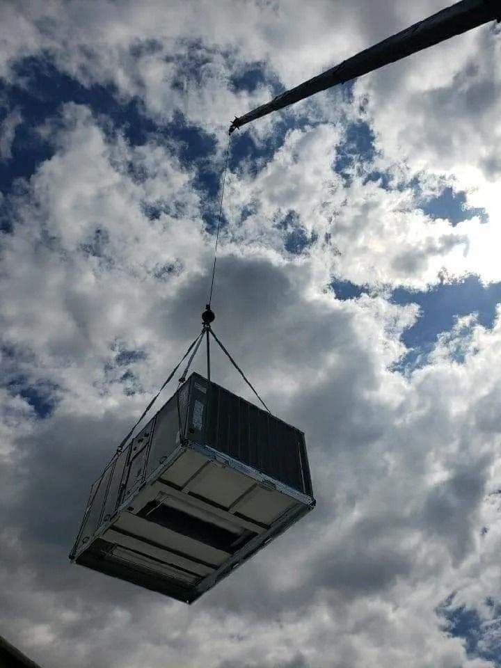 Crane lifting large HVAC unit against a cloudy sky.