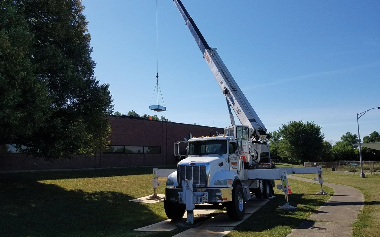 A crane lifting a round, silver object near a building on a sunny day.