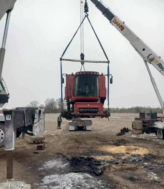 Crane lifting a red combine, likely for repair, in a field.