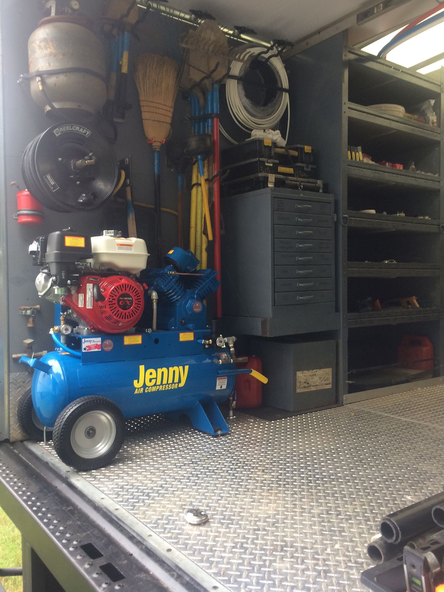 A blue Jenny air compressor inside a service truck with metal shelves, tools, and equipment mounted on the walls.