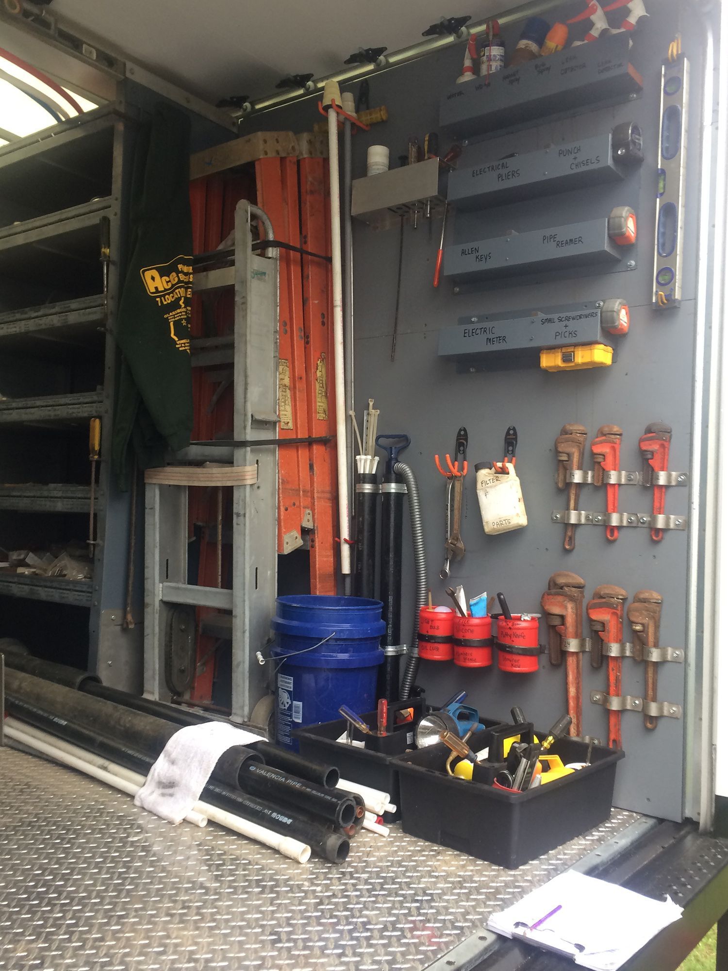 Interior of a work truck featuring shelves, hanging pipe wrenches, organized tools, and a ladder stored in the back.