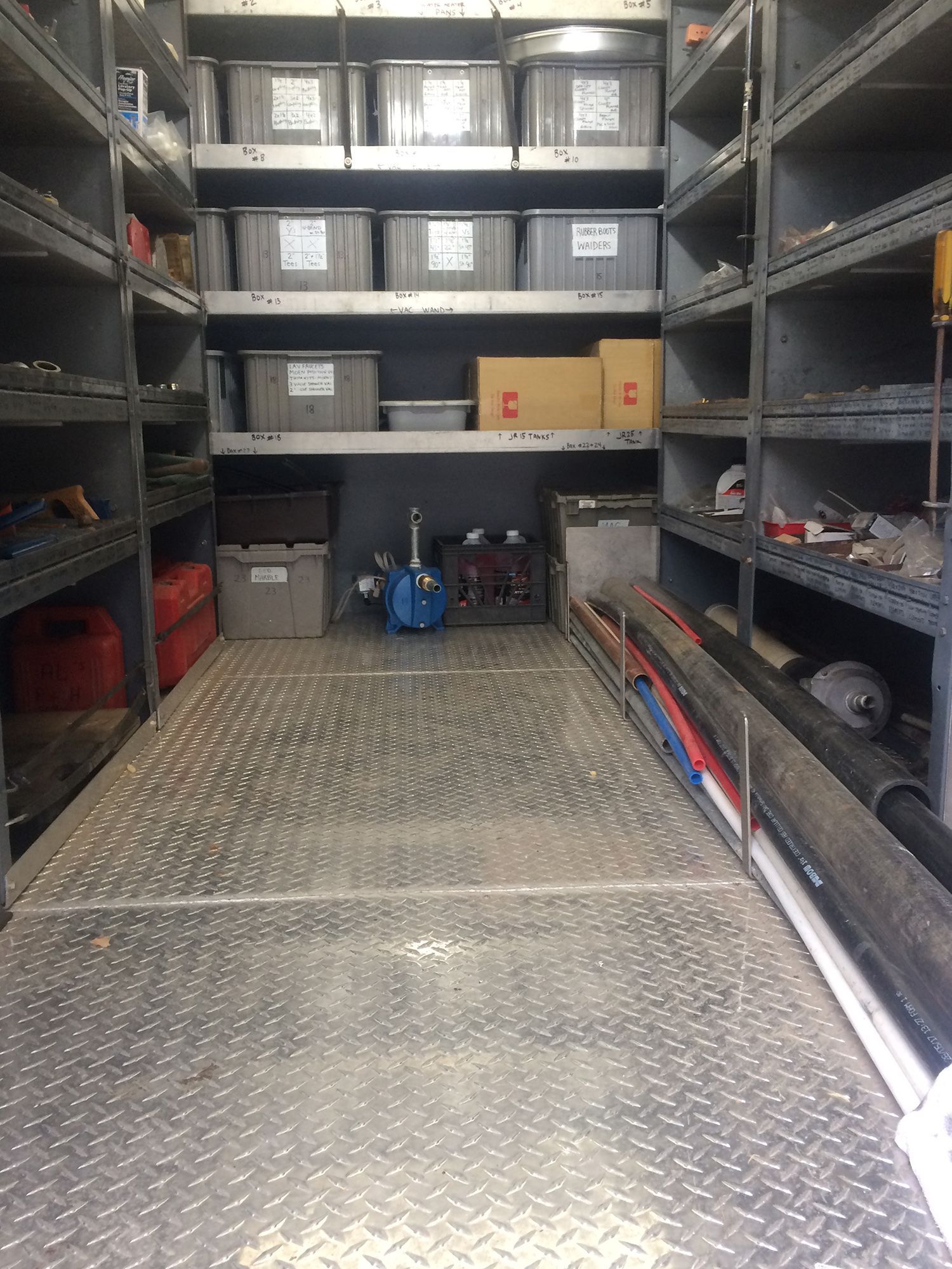 Interior of a utility van featuring metal shelving units filled with plastic storage bins, equipment, and supplies.
