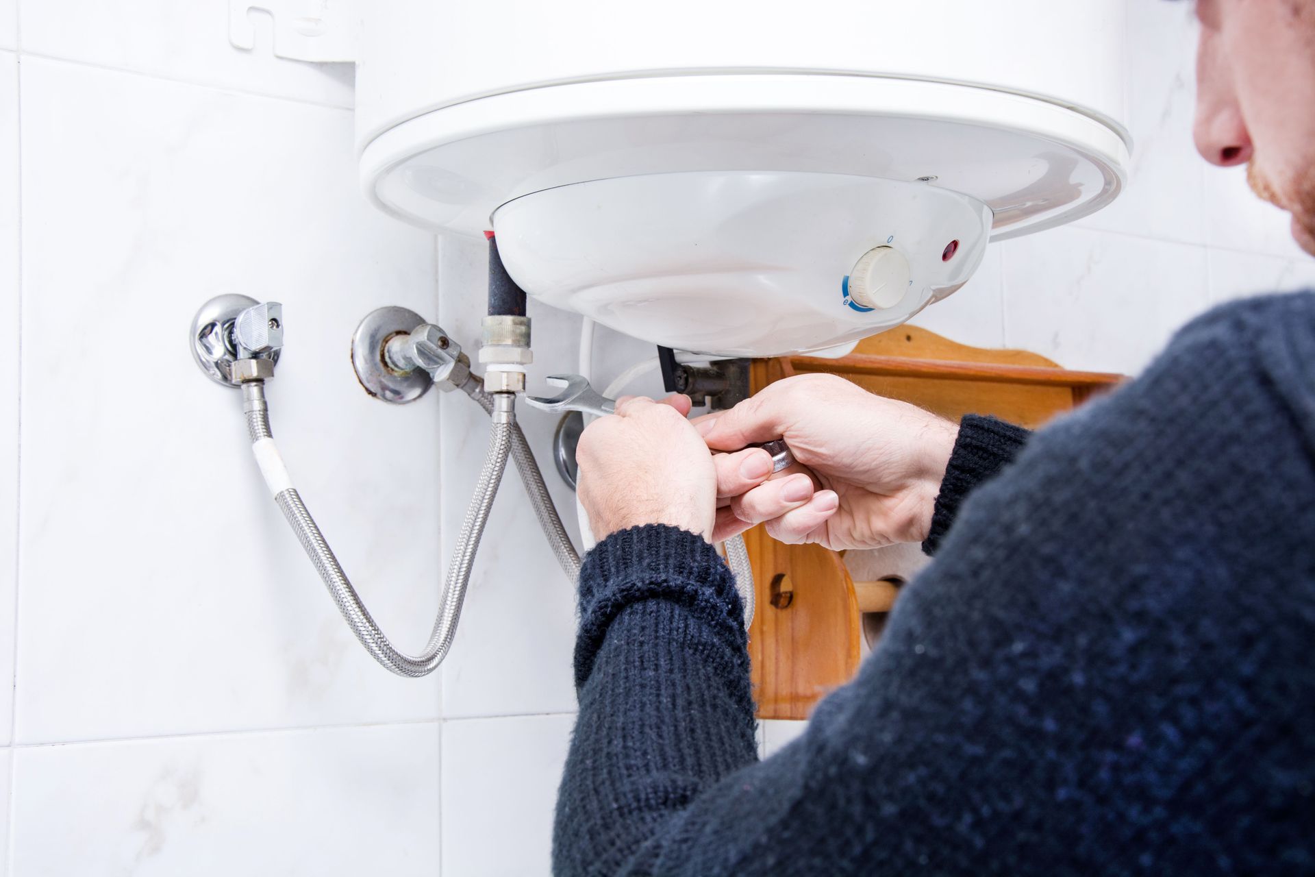 A person using a wrench to repair the plumbing connections on a wall-mounted electric water heater.