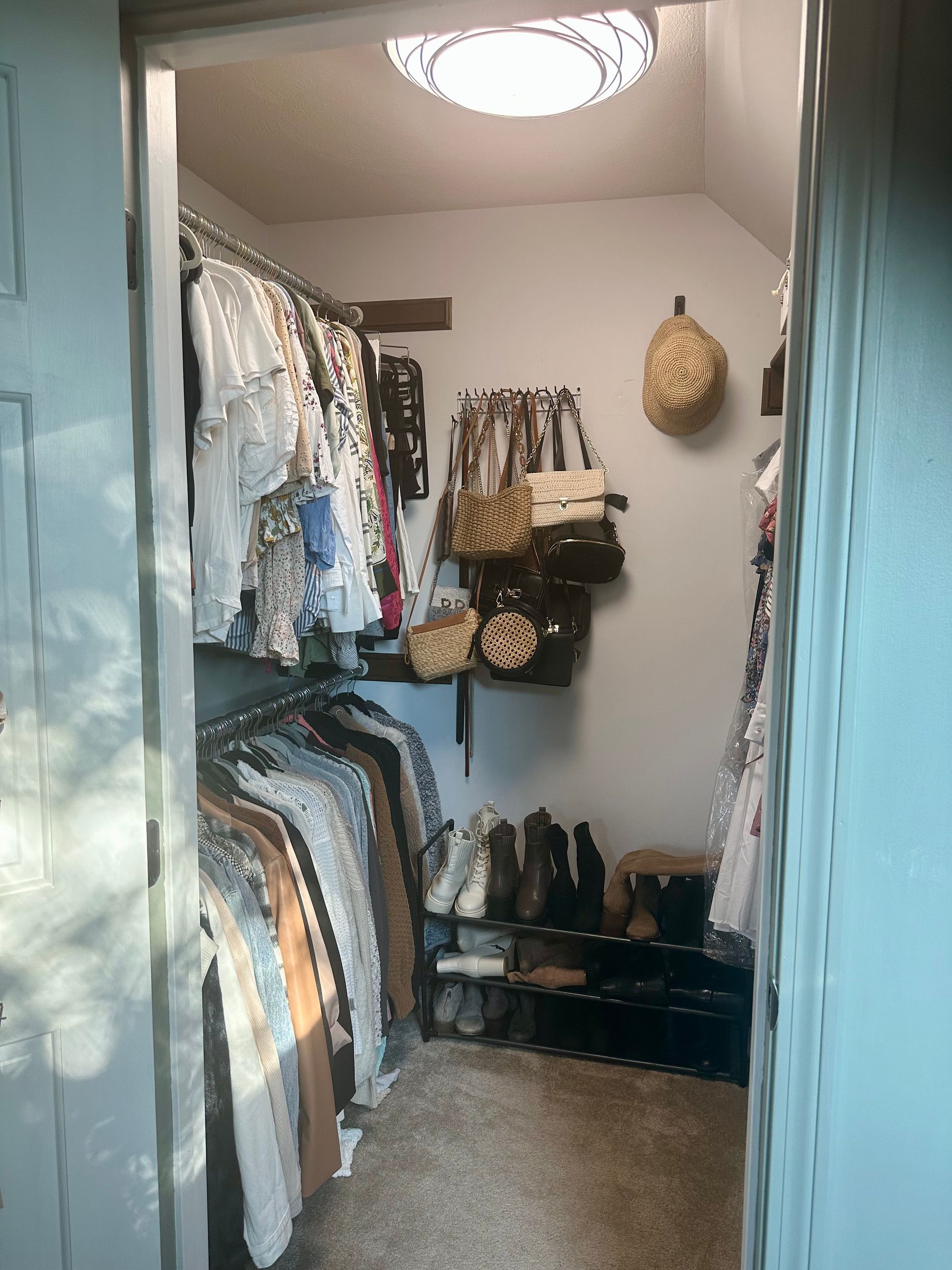 small walk in closet with hanging clothes, shoes and bags