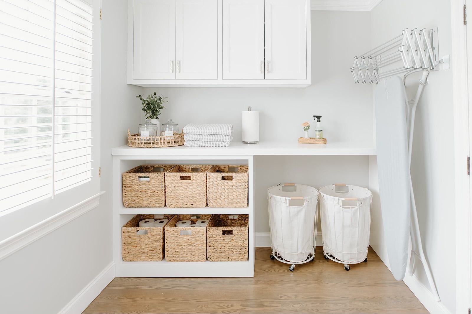 A laundry room with white cabinets, wicker baskets, and a window