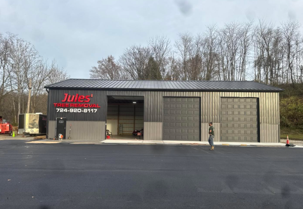 Small gray auto repair shop with red sign, garage doors, and parked cones on an empty lot