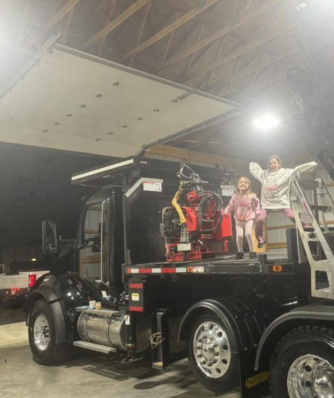 Children posing on a flatbed tow truck under a lit canopy at night