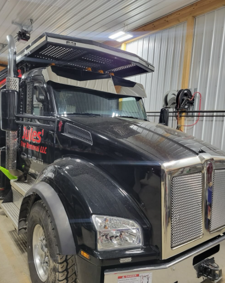 Black semi-truck with chrome grille parked inside a metal garage or workshop.
