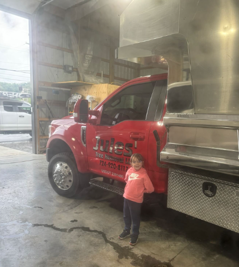 Child standing beside a red delivery truck at a covered car wash, with spray mist in the air.