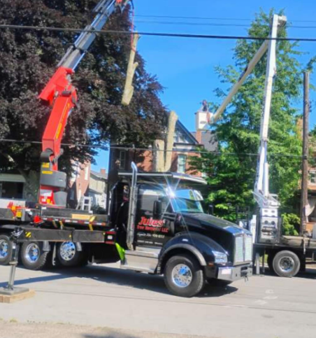 Tow truck with raised crane lifting a white utility truck on a sunny street.