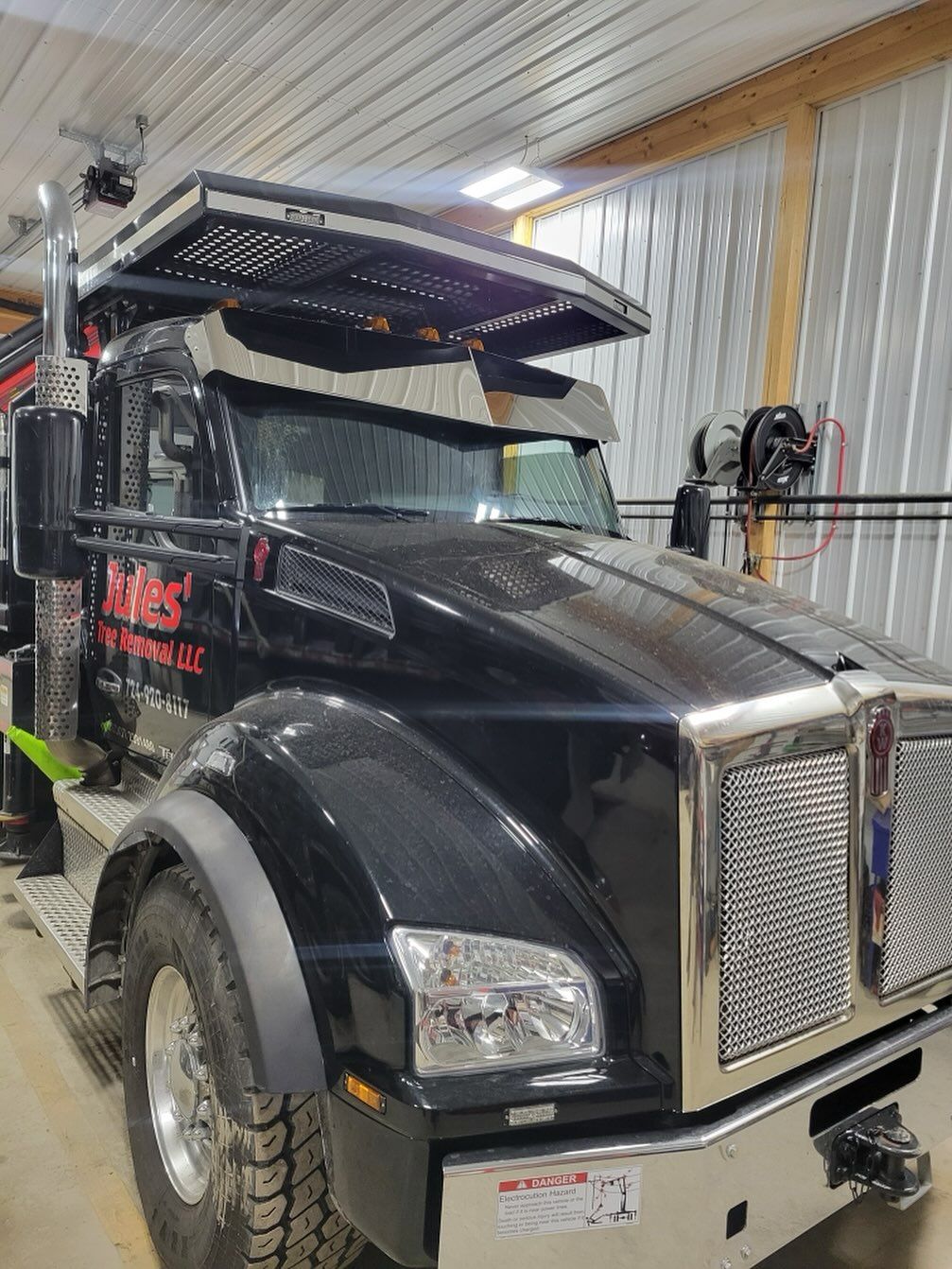 Black semi truck with chrome grille parked inside a workshop or garage.