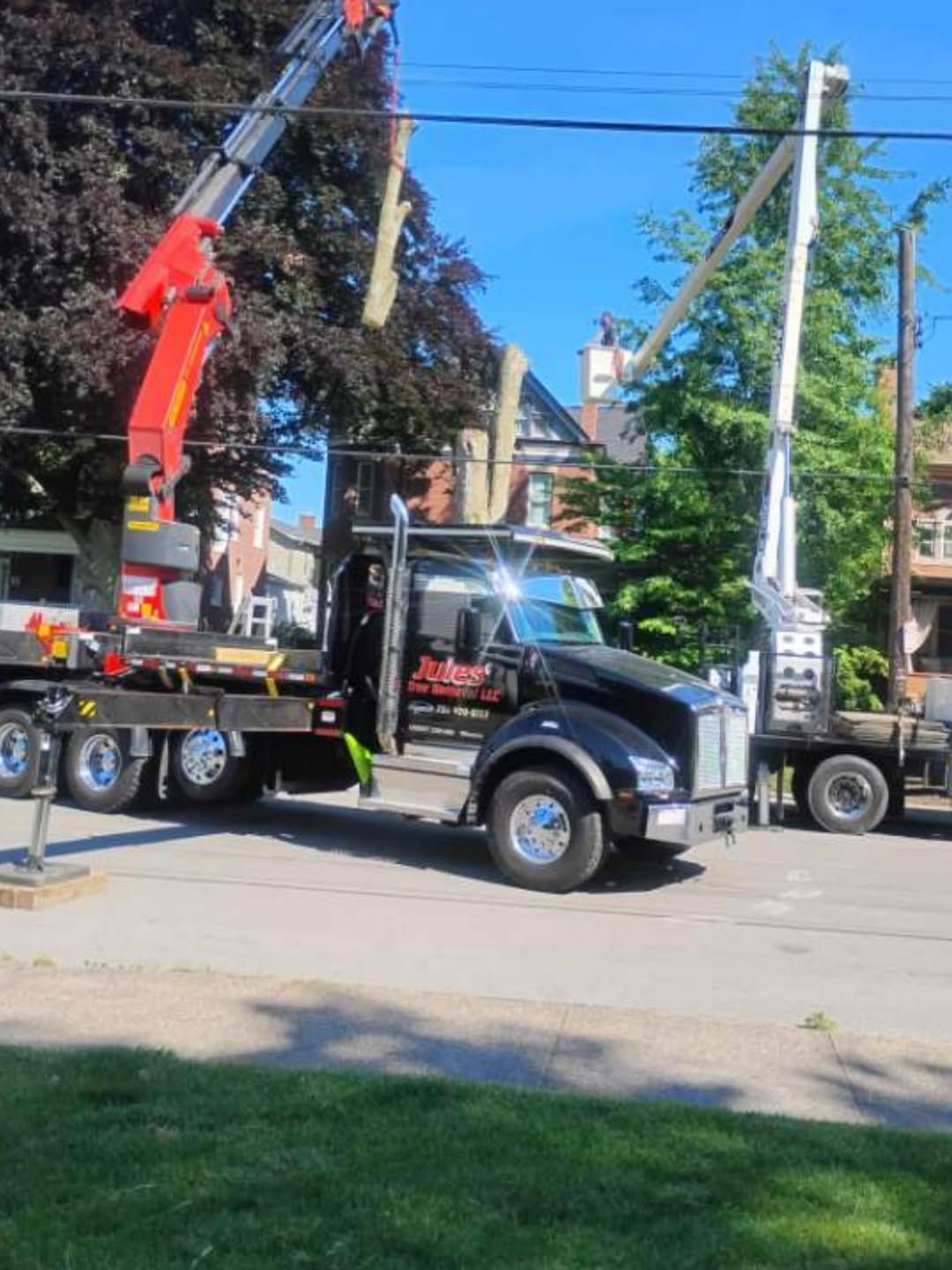Tow truck with raised red crane parked on a sunny residential street under blue sky.