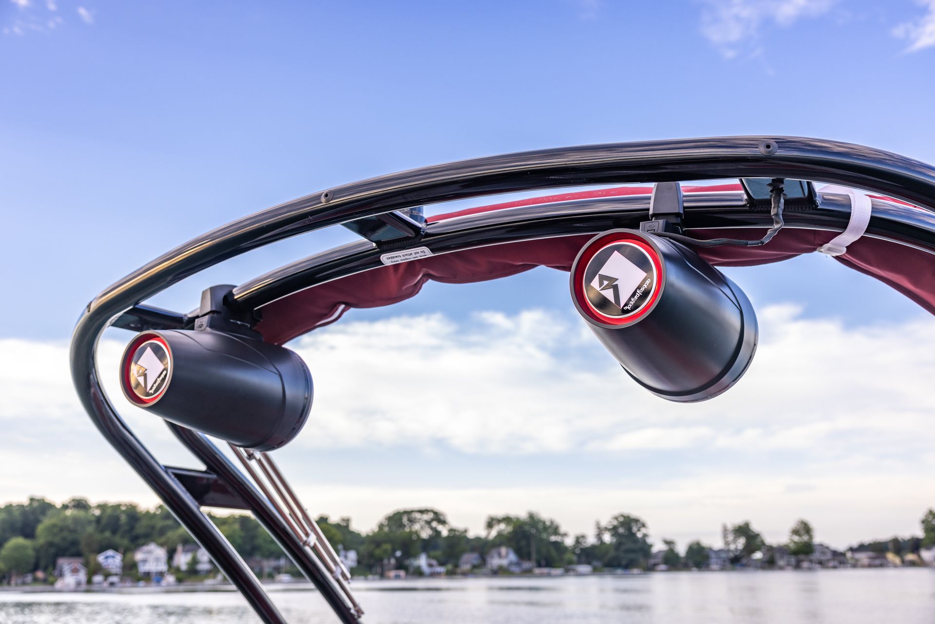 Close-up of a wakeboard boat tower with black speakers and a lake in the background