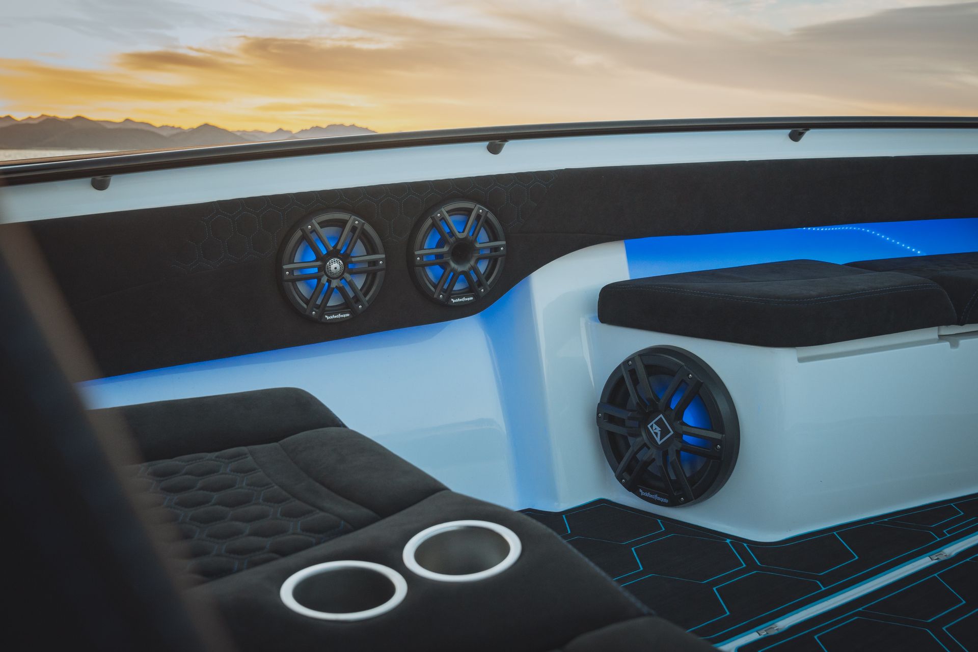 Modern boat cabin with white seating, blue lighting, speakers, and sunset view outside the window