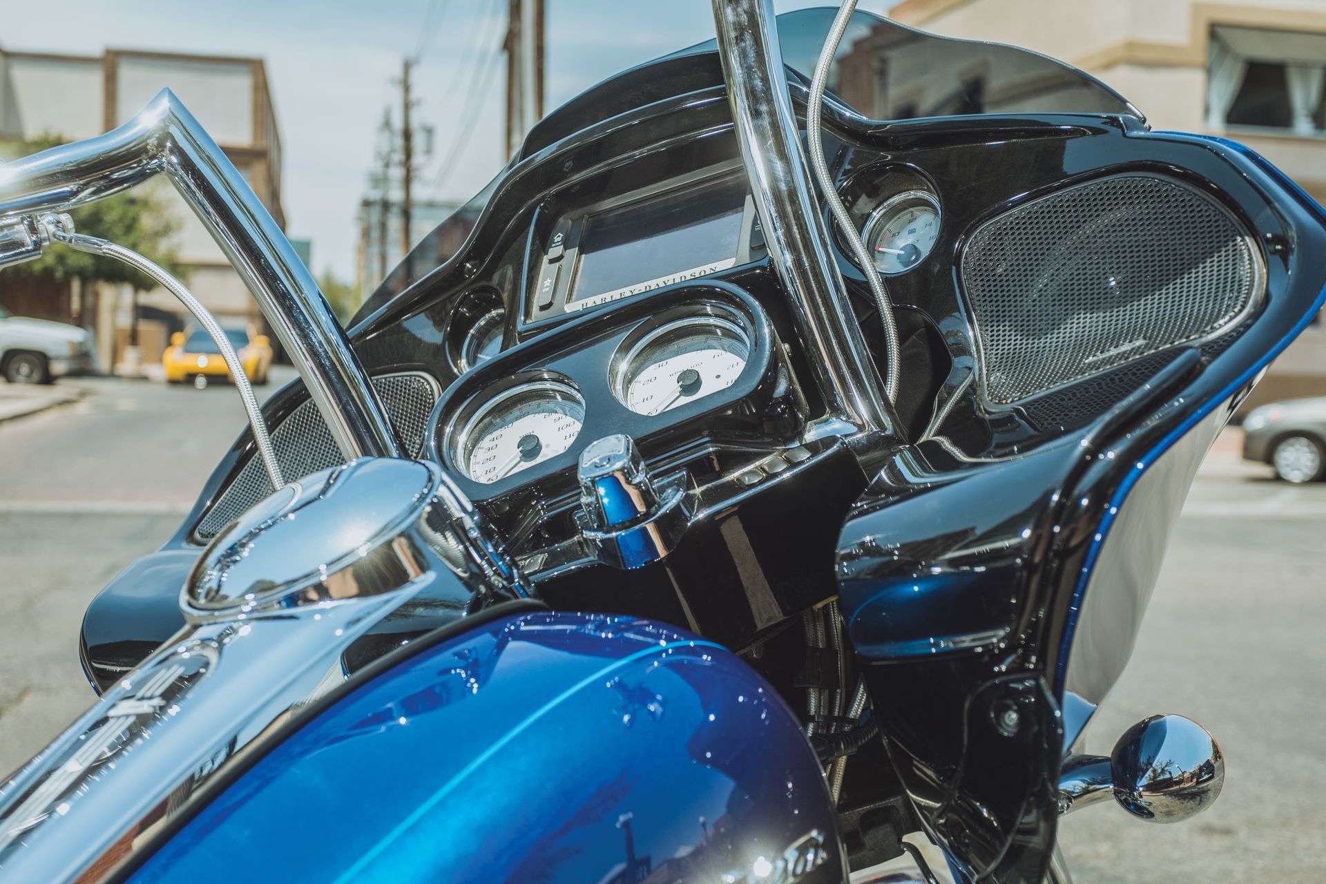 Blue motorcycle dashboard and windshield with chrome handlebars parked outdoors