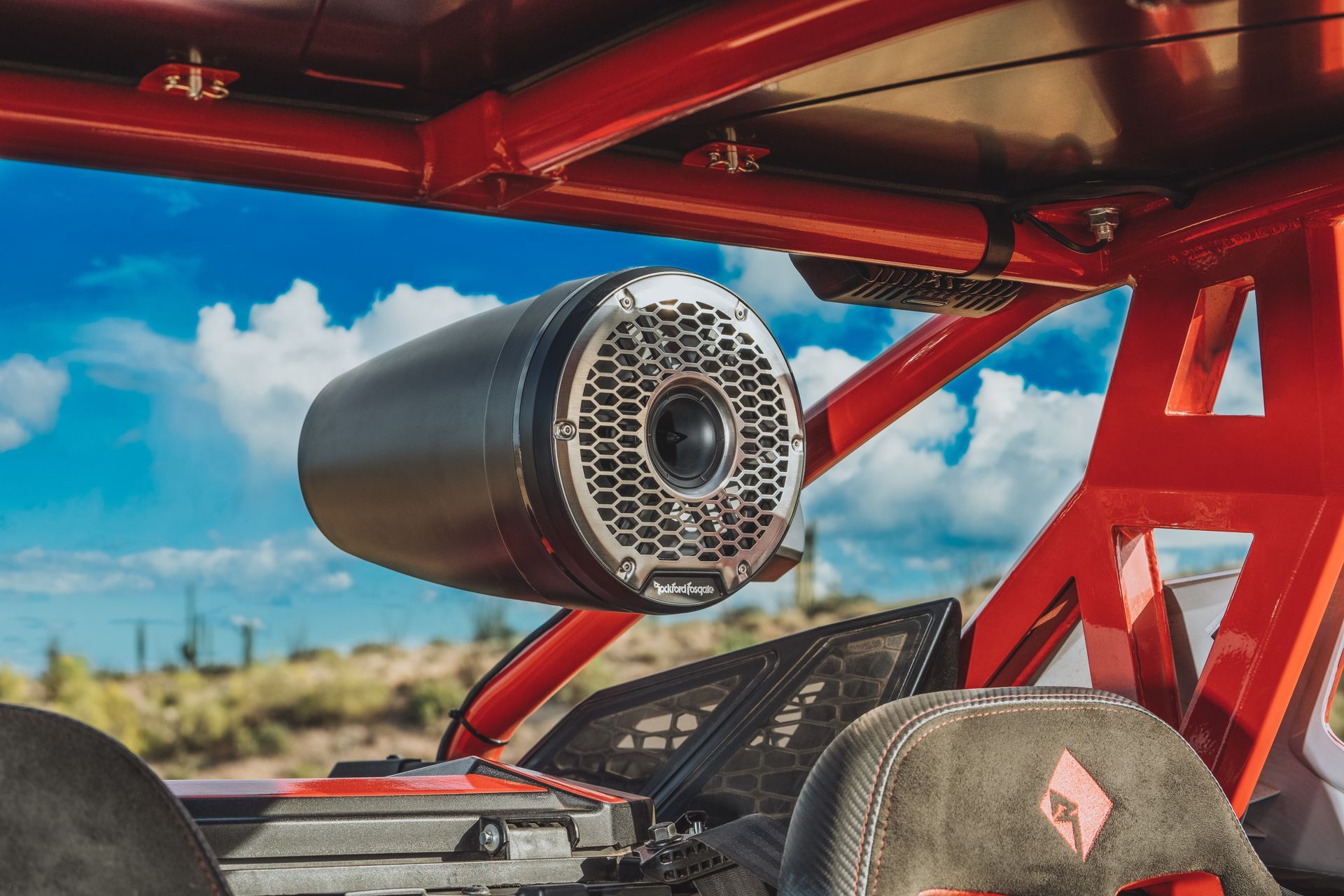 Red off-road vehicle interior with a mounted black cylindrical loudspeaker against a blue sky