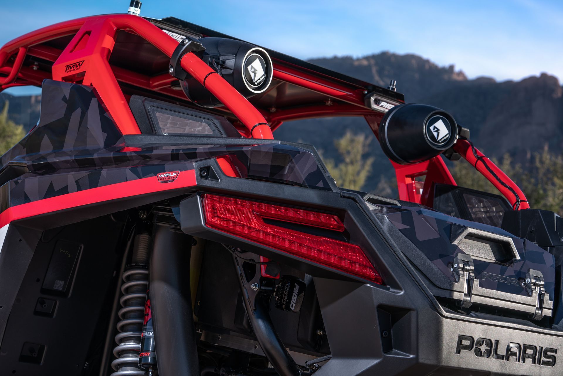 Red Polaris off-road vehicle with roll cage and roof lights on rocky terrain at sunset