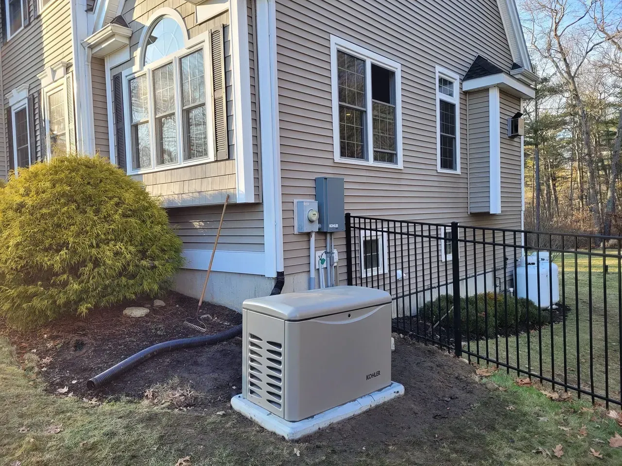 A generator is sitting in front of a house next to a fence.