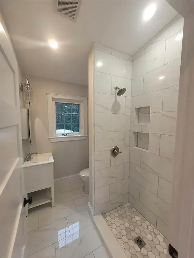 A bathroom with a walk in shower, toilet, sink, and window.