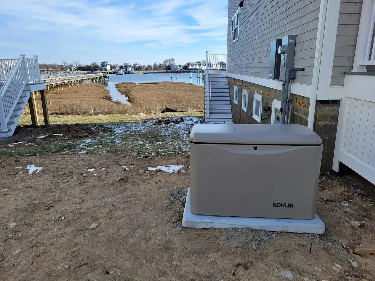 A generator is sitting in the dirt in front of a house.