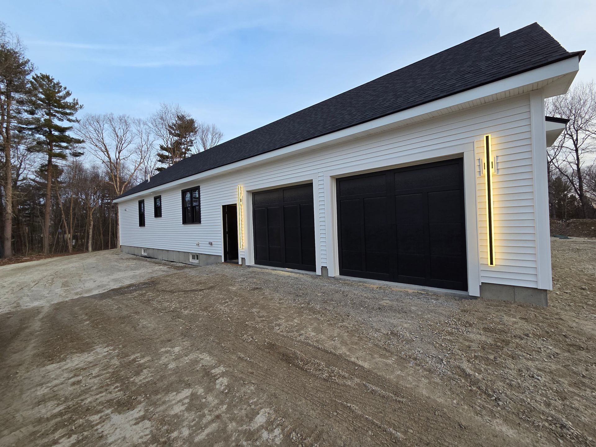 A white house with black garage doors is sitting on top of a dirt hill.