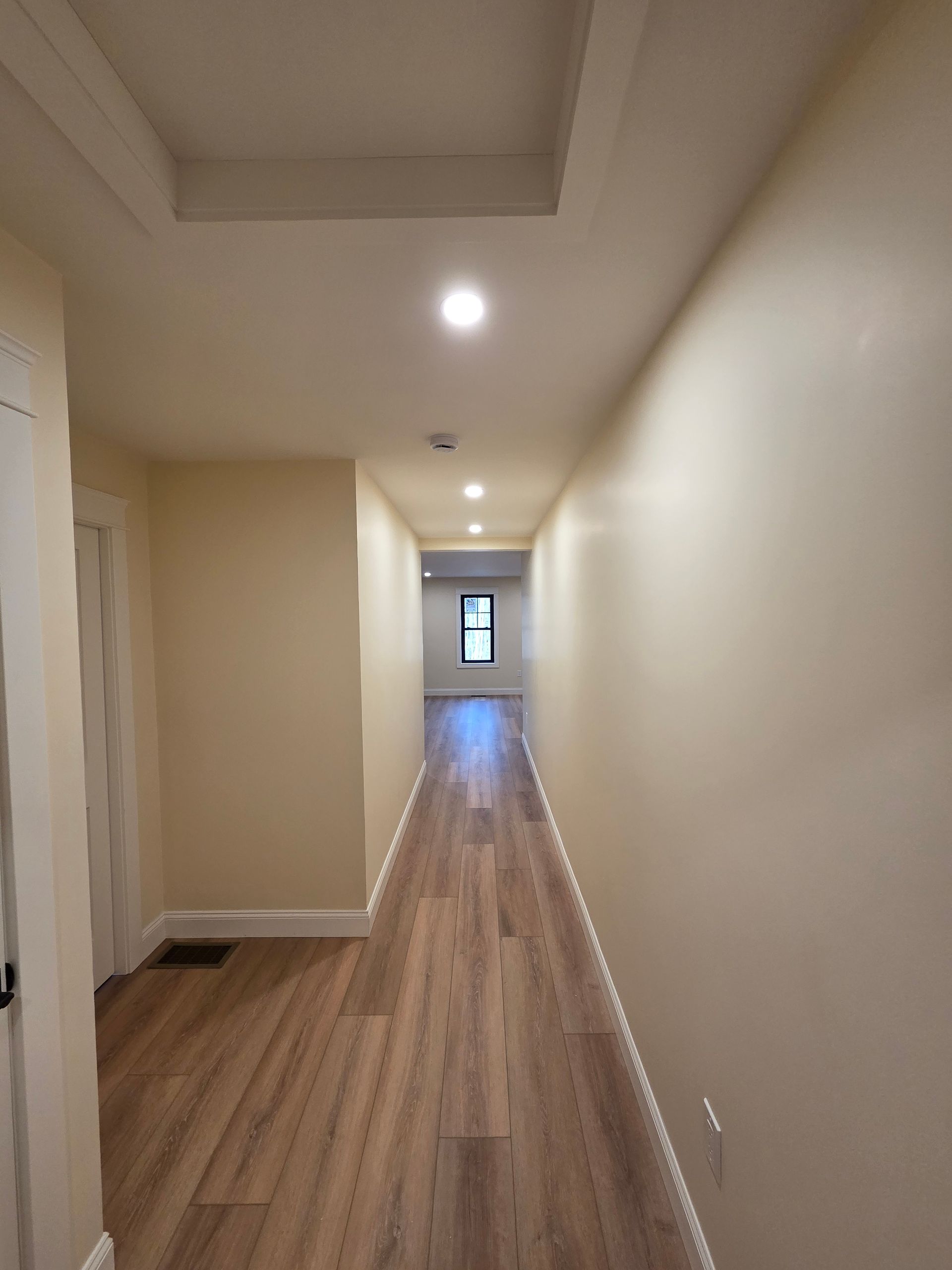 A long hallway with hardwood floors and white walls in a house.